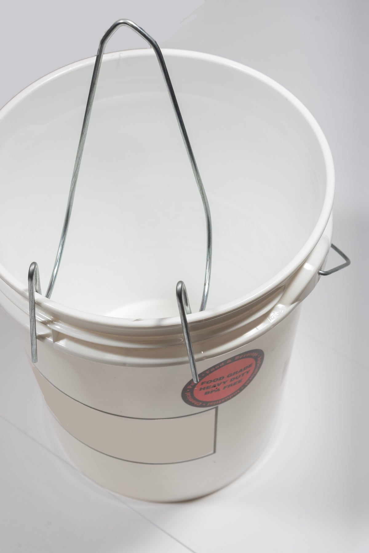 A white bucket attached with an unloader: long thick piece of metal bent in three places and rounded out made to hook onto the edge of a bucket.